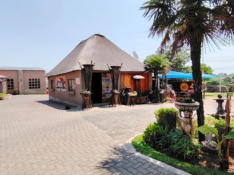 Commercial property exterior featuring a traditional thatch-roof building, paved driveway, and landscaped garden area with a stone fountain.