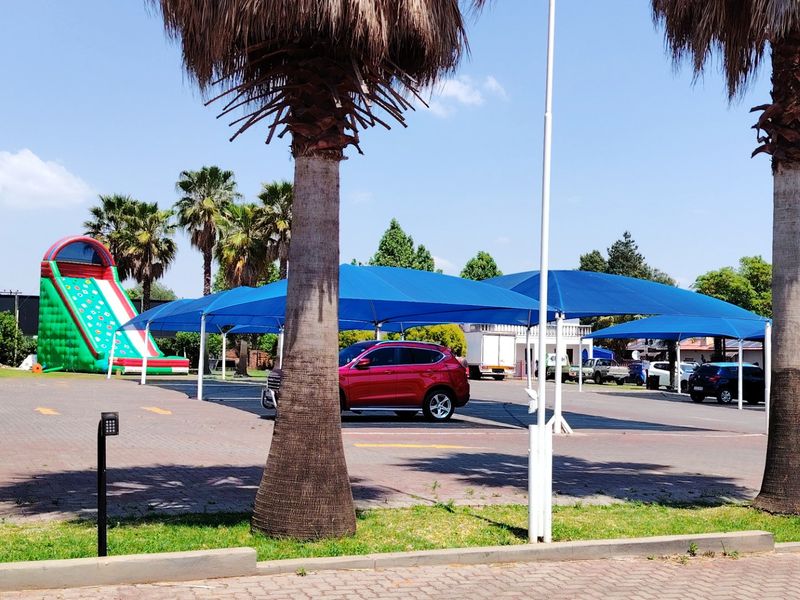 Commercial parking area featuring paved surfaces, multiple shade cloth structures, and established palm trees.
