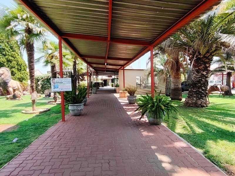 A covered paved walkway leads through a well-maintained garden area with mature palm trees and lawn.