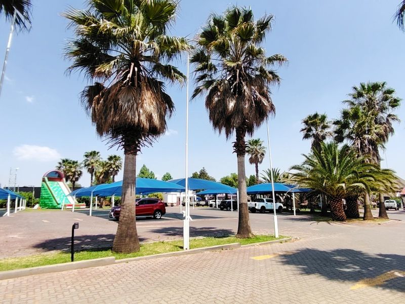 Commercial property exterior featuring a large paved parking area with blue shade cloth carports and mature palm trees.
