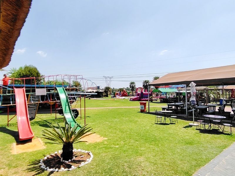 Outdoor commercial recreational area featuring a covered seating space, manicured lawn, and playground facilities, suitable for family-oriented events or hospitality use.
