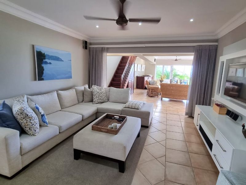 Spacious open-plan living area featuring tiled flooring, recessed ceiling lighting, a ceiling fan, and a built-in media unit, flowing into an adjacent sunroom.