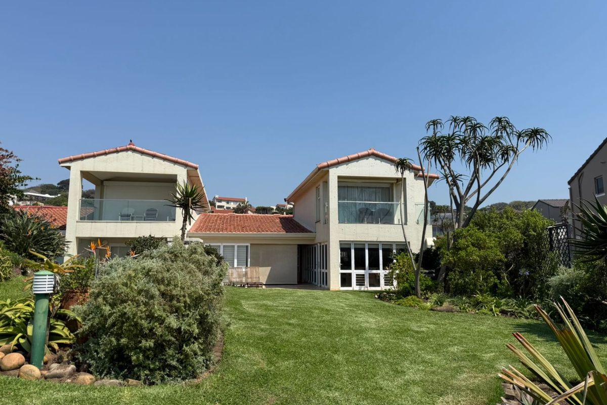 Rear view of the townhouse featuring a landscaped garden, upper-level balconies with glass balustrades, and tiled roof architecture.