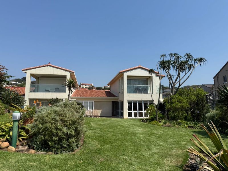Rear view of the townhouse featuring a landscaped garden, upper-level balconies with glass balustrades, and tiled roof architecture.