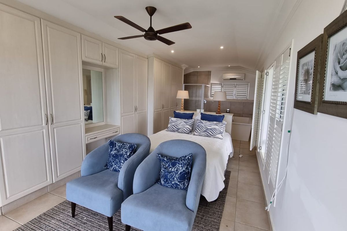 Spacious bedroom featuring extensive built-in cabinetry, a vanity area, ceiling fan, and an en-suite bathroom layout with tiled flooring.