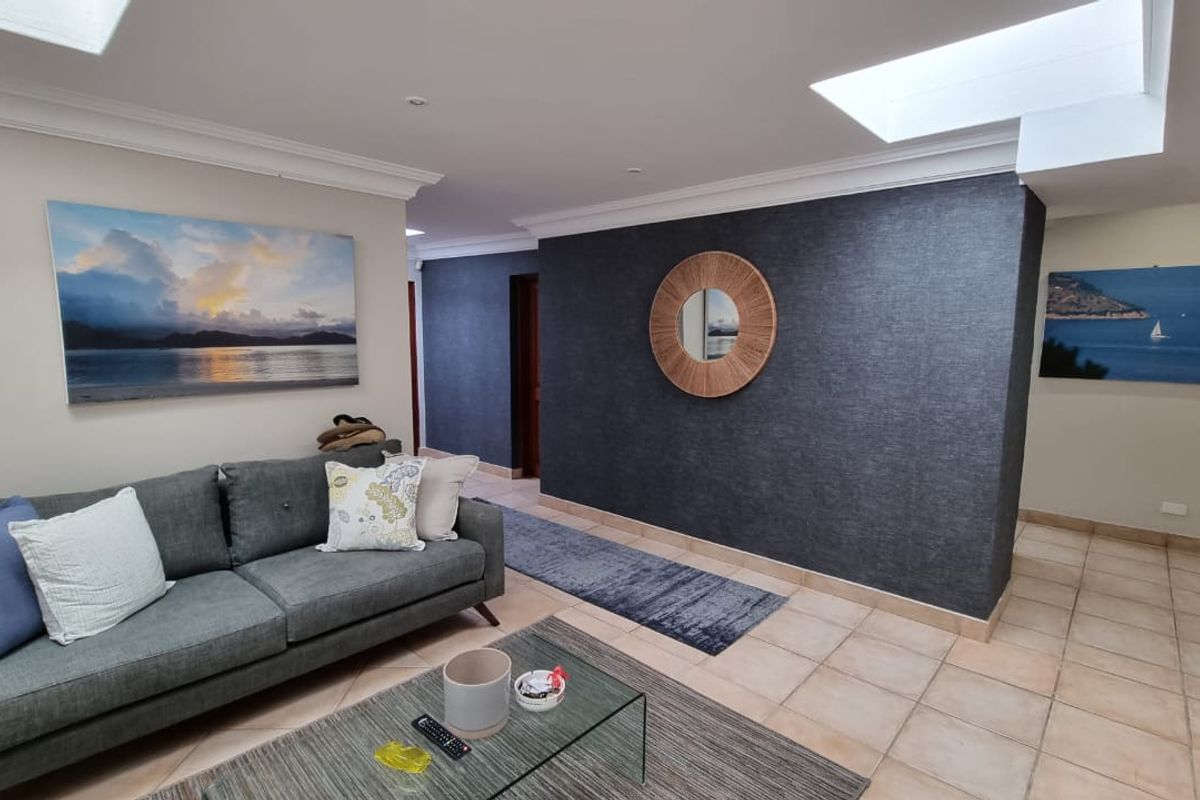 A spacious living area featuring tiled flooring, recessed skylights, and a striking dark textured feature wall.