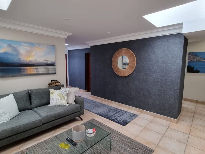 A spacious living area featuring tiled flooring, recessed skylights, and a striking dark textured feature wall.