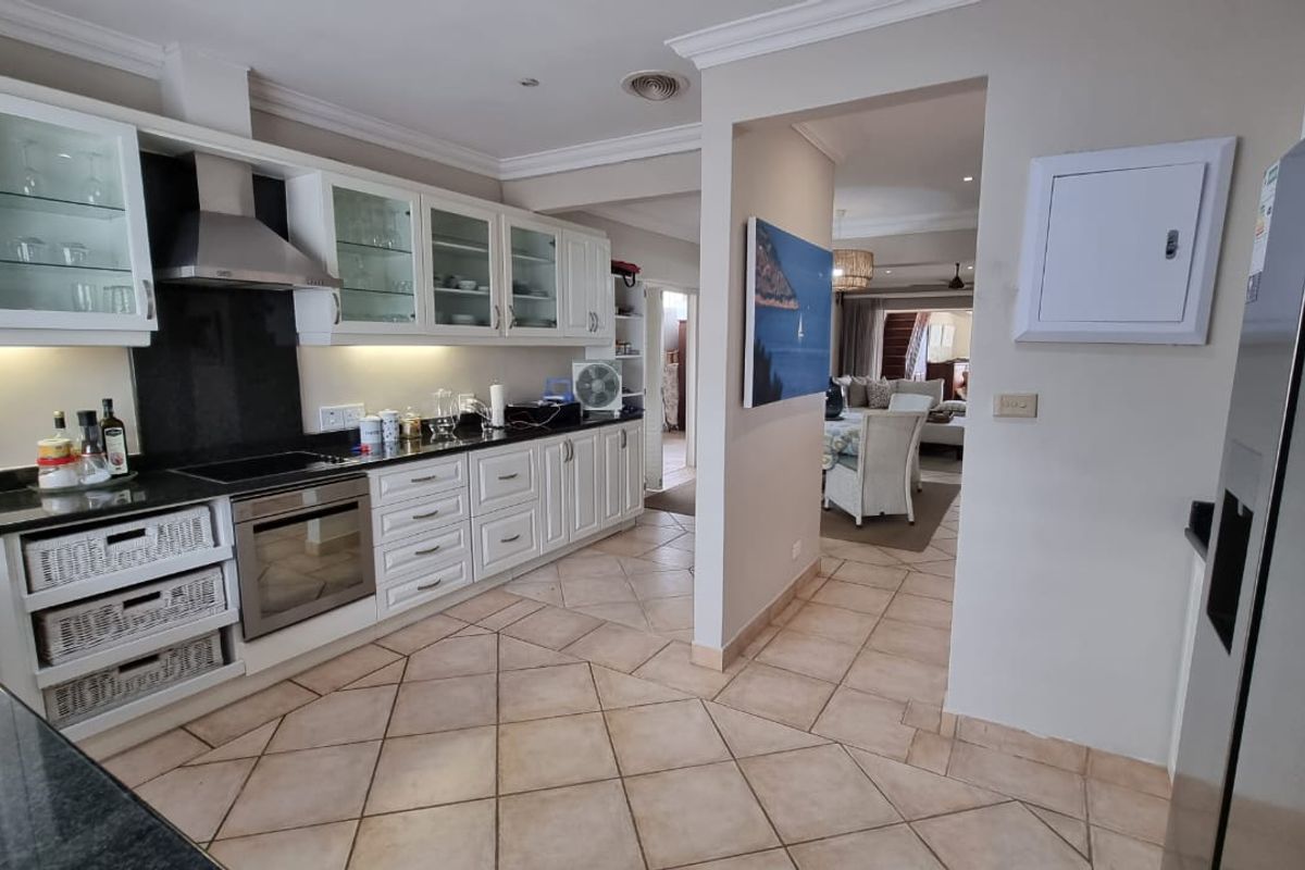 A well-appointed kitchen featuring white cabinetry, dark granite countertops, a built-in oven, and an extractor fan, flowing into an adjacent living area.