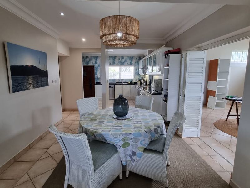 Open-plan dining area flowing into a functional kitchen with white cabinetry, tiled flooring, and recessed ceiling lighting.