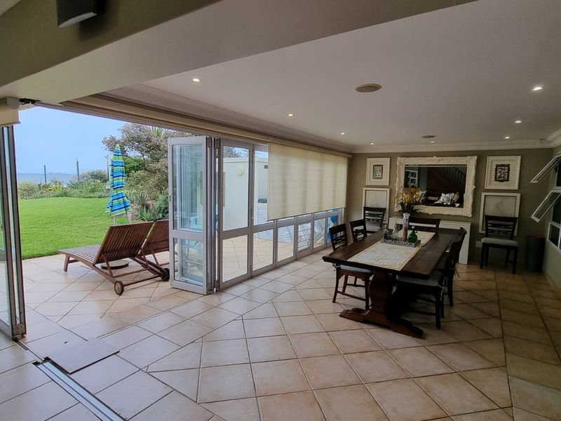 Spacious open-plan living and dining area featuring large stackable glass doors that open onto a paved patio and garden with ocean views.