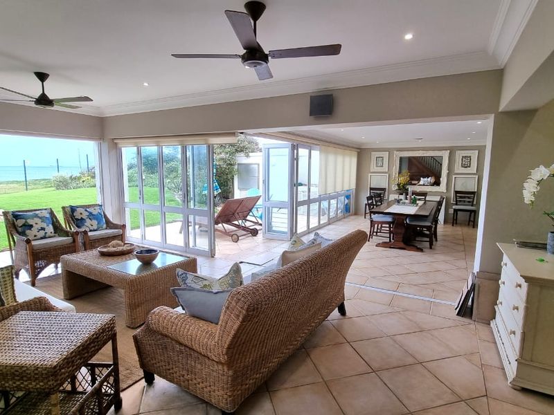 Spacious open-plan living and dining area featuring large glass stacker doors that open onto a patio with garden and ocean views.