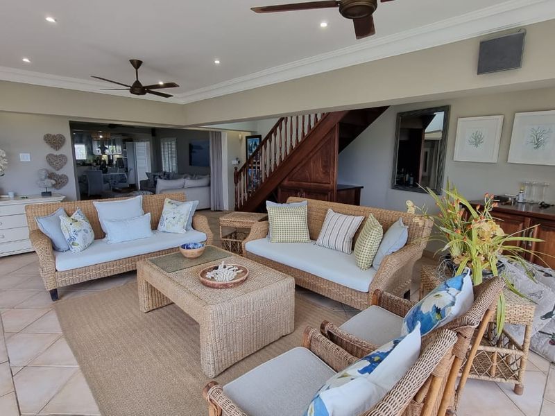 Spacious open-plan living area featuring tiled flooring, recessed ceiling lighting, ceiling fans, and a wooden staircase leading to the upper level.