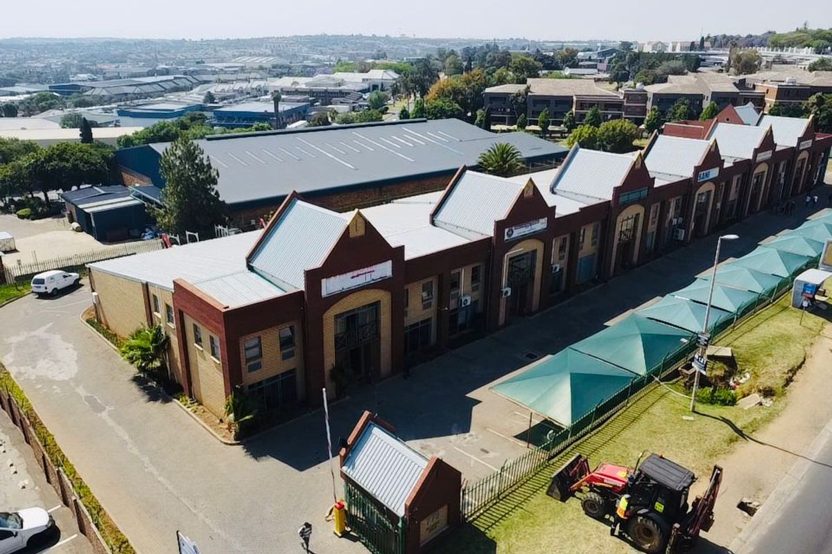 Aerial view of an industrial complex featuring multiple brick units with metal roofing, a security gatehouse, and dedicated shade-covered parking areas.
