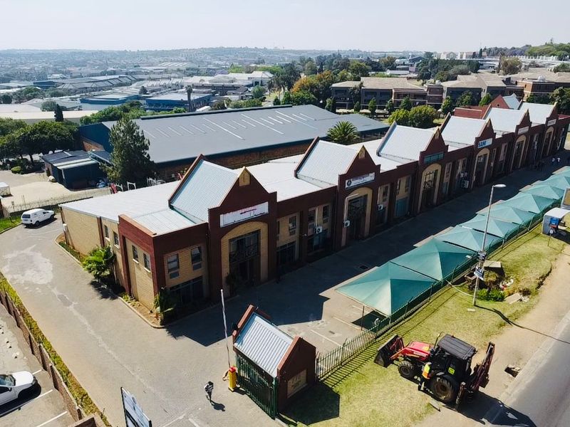Aerial view of an industrial complex featuring multiple brick units with metal roofing, a security gatehouse, and dedicated shade-covered parking areas.