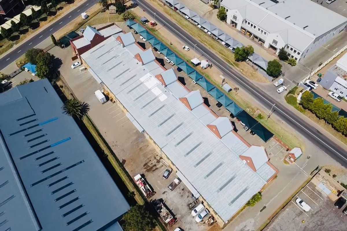 Aerial view of an industrial property featuring a large metal-roofed warehouse building with adjacent asphalt parking and covered parking bays.