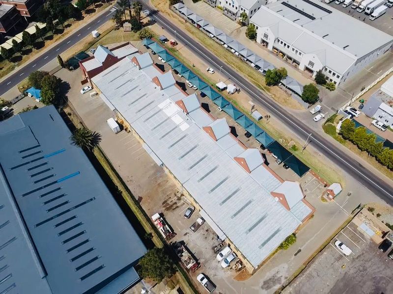 Aerial view of an industrial property featuring a large metal-roofed warehouse building with adjacent asphalt parking and covered parking bays.