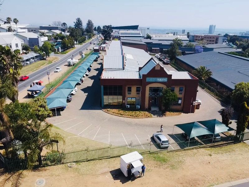Aerial view of an industrial property featuring a brick office building, extensive paved parking with shade cloth carports, and secure perimeter fencing.