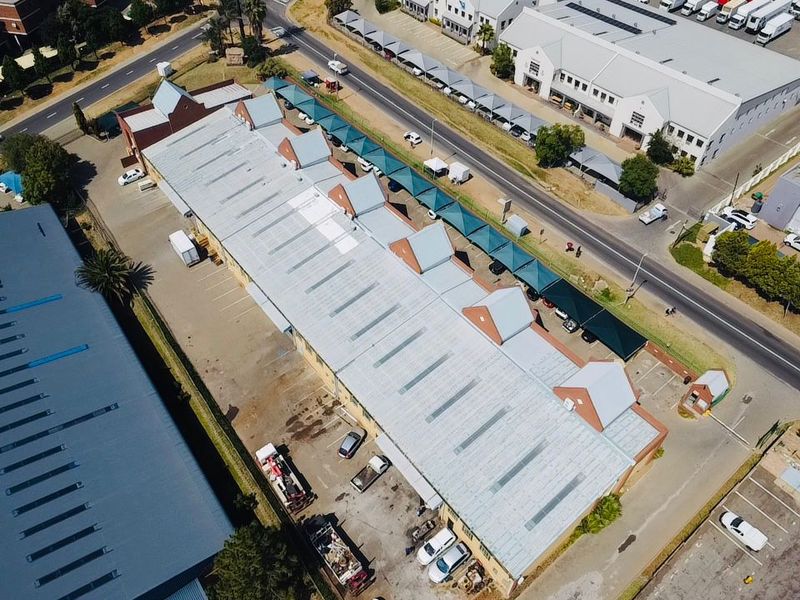 Aerial view of an industrial property featuring a large metal-roofed warehouse, dedicated parking areas, and covered vehicle bays.