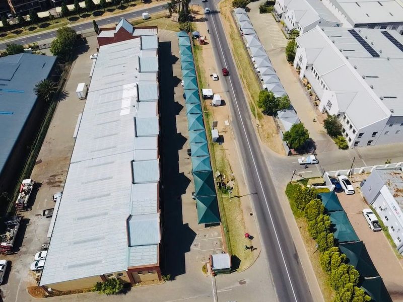 Aerial view of an industrial property complex featuring large warehouse buildings, extensive paved parking areas, and rows of shade cloth carports.