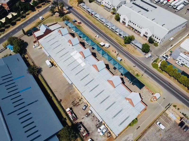 Aerial view of an industrial property featuring a large warehouse building with a metal roof and extensive paved parking facilities.