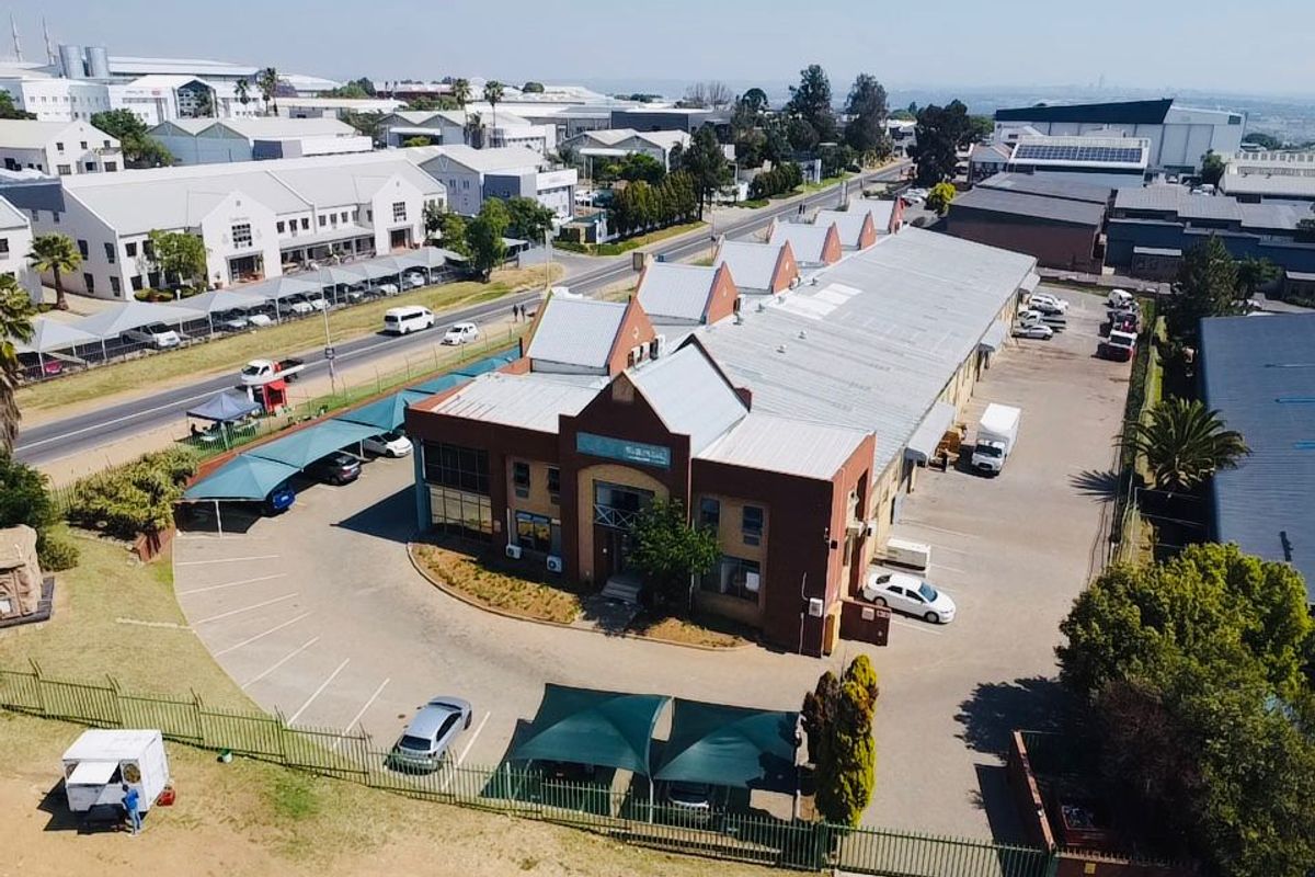 Aerial view of an industrial property featuring a main building with a metal roof, extensive paved parking, and shade cloth carports.