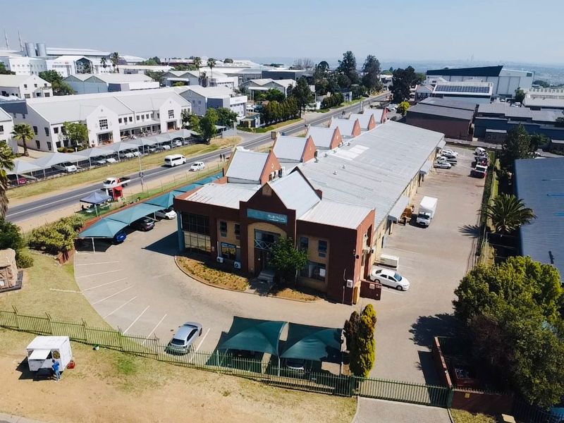 Aerial view of an industrial property featuring a main building with a metal roof, extensive paved parking, and shade cloth carports.