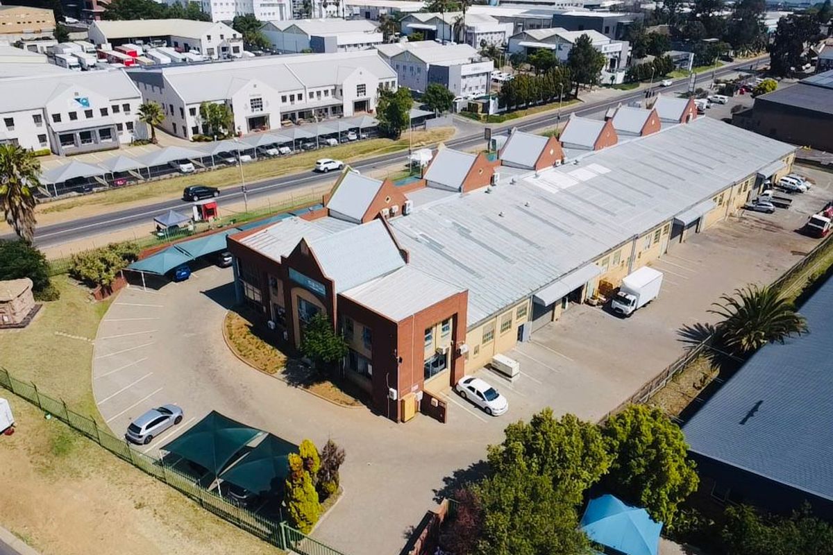 Aerial view of an industrial property featuring a large warehouse building with a metal roof, brick facade, and extensive paved parking facilities.