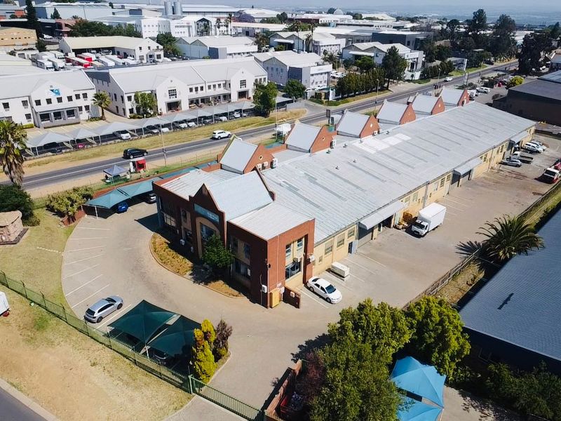Aerial view of an industrial property featuring a large warehouse building with a metal roof, brick facade, and extensive paved parking facilities.