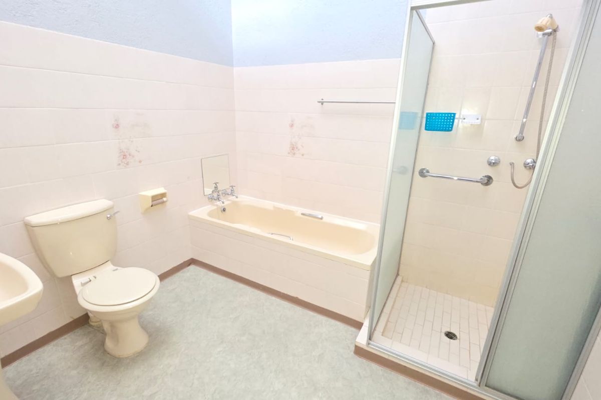 A dated bathroom featuring a separate bathtub, shower enclosure, pedestal basin, and toilet, requiring cosmetic updates to modernize the space.