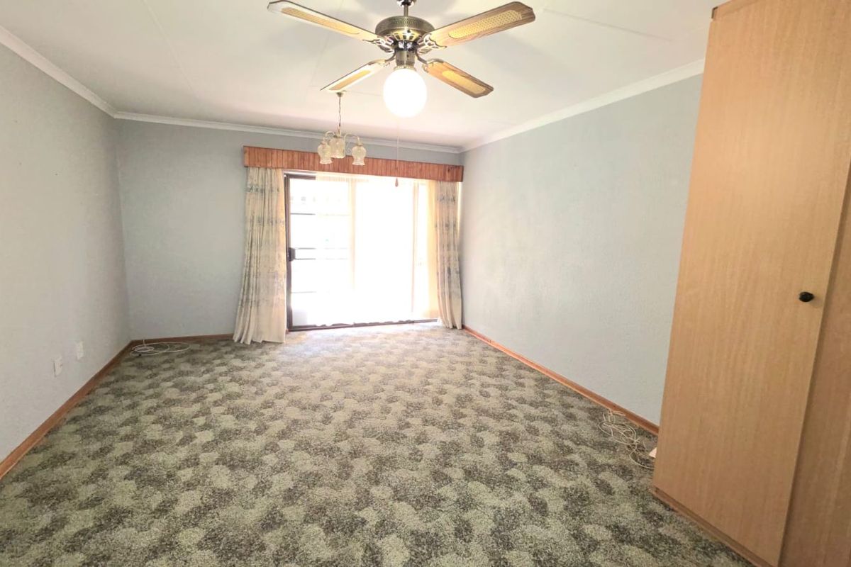 A spacious bedroom featuring a ceiling fan, built-in wardrobe, and sliding glass door access to the exterior, finished with patterned carpet flooring.