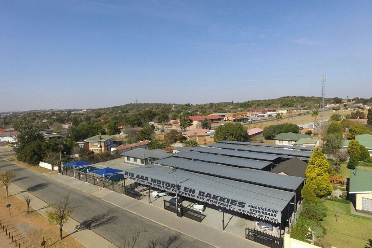 Aerial view of a commercial vehicle dealership property featuring extensive metal carport structures, paved parking areas, and secure perimeter fencing.