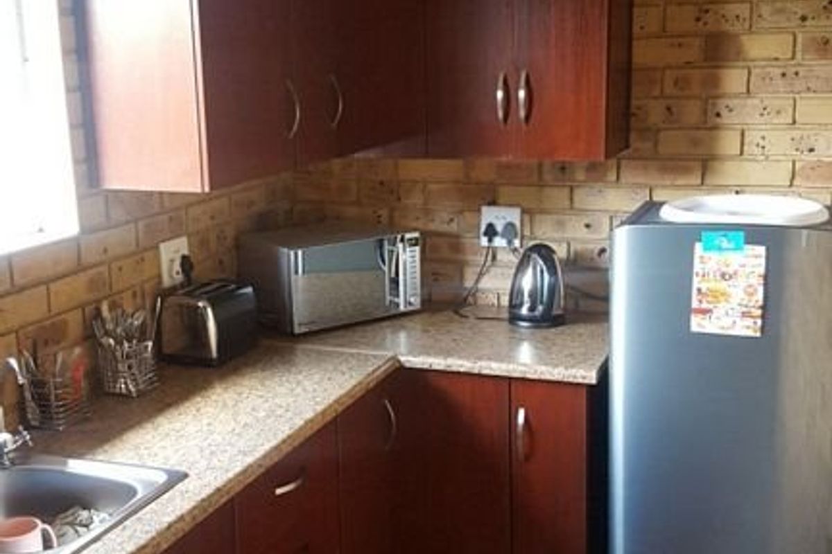A functional kitchen featuring dark wood-look cabinetry, granite-style countertops, exposed brick walls, and ceramic floor tiling.