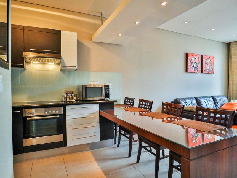 Modern open-plan kitchen and dining area featuring sleek cabinetry, integrated appliances, tiled flooring, and recessed ceiling lighting, creating a functional and cohesive living space.