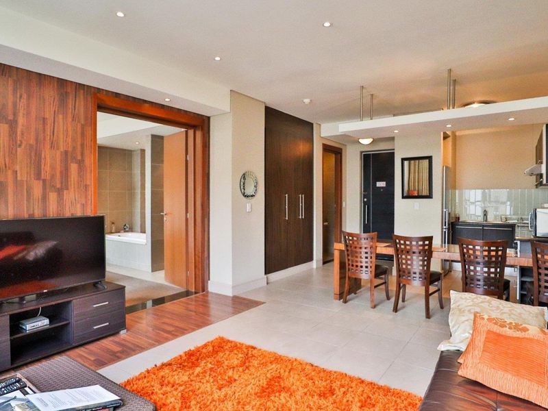 Open-plan living and dining area featuring a modern kitchen, wood-accented flooring, and direct access to an adjoining bathroom.