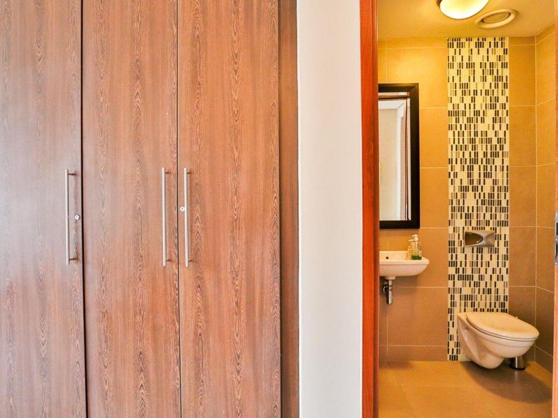 A clean bathroom featuring a wall-mounted toilet, basin, and a decorative mosaic tile accent wall, adjacent to built-in wooden storage cupboards.