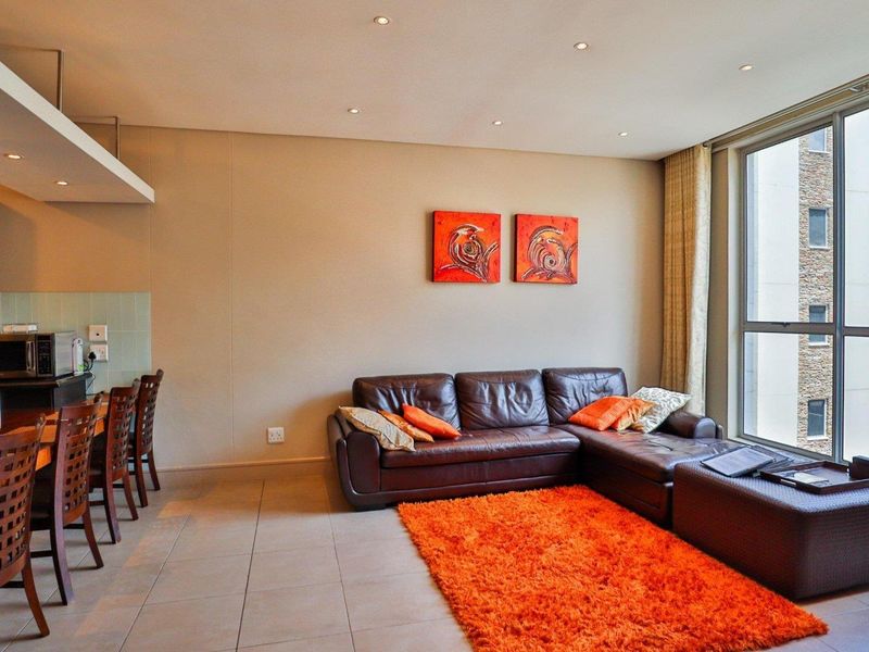 A bright open-plan living and kitchen area featuring tiled floors, recessed lighting, and large windows providing ample natural light.