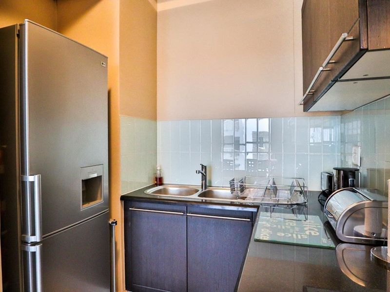 Compact kitchen featuring dark cabinetry, a double sink with mixer tap, and a light-toned tiled splashback.