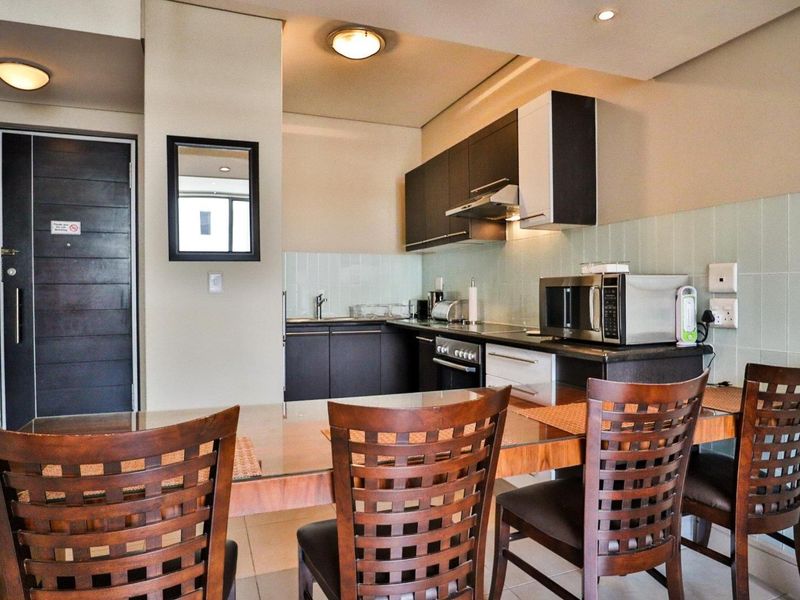 Open-plan kitchen and dining area featuring dark cabinetry, integrated appliances, tiled backsplash, and modern recessed lighting.