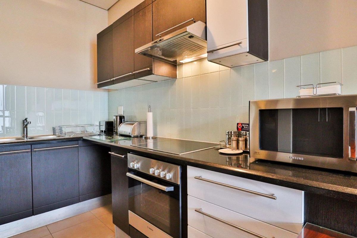 Modern kitchen featuring dark and white cabinetry, granite countertops, integrated electric hob, oven, extractor fan, and a clean tiled backsplash.