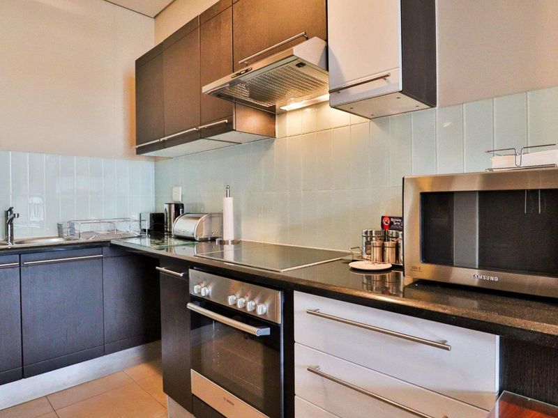 Modern kitchen featuring dark and white cabinetry, granite countertops, integrated electric hob, oven, extractor fan, and a clean tiled backsplash.