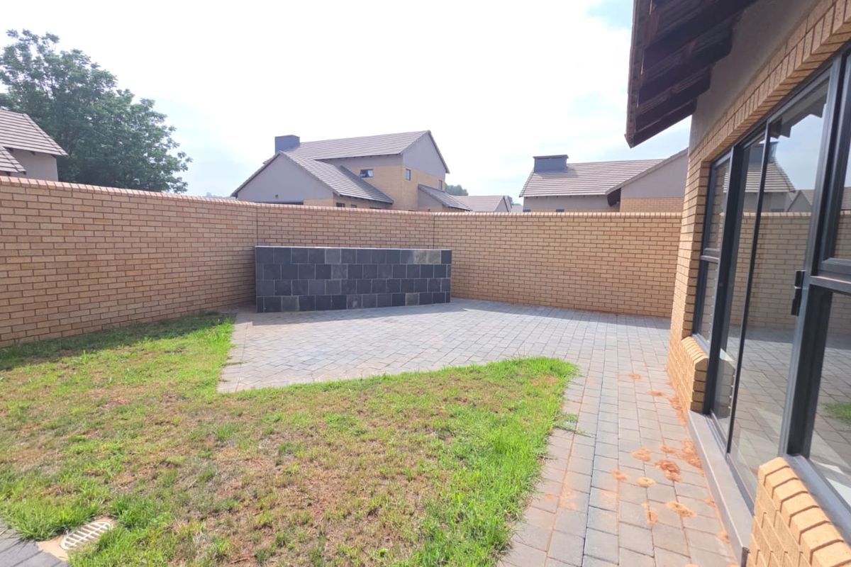 A private rear garden featuring a paved patio area, a built-in brick braai or feature wall, and a perimeter brick boundary wall.