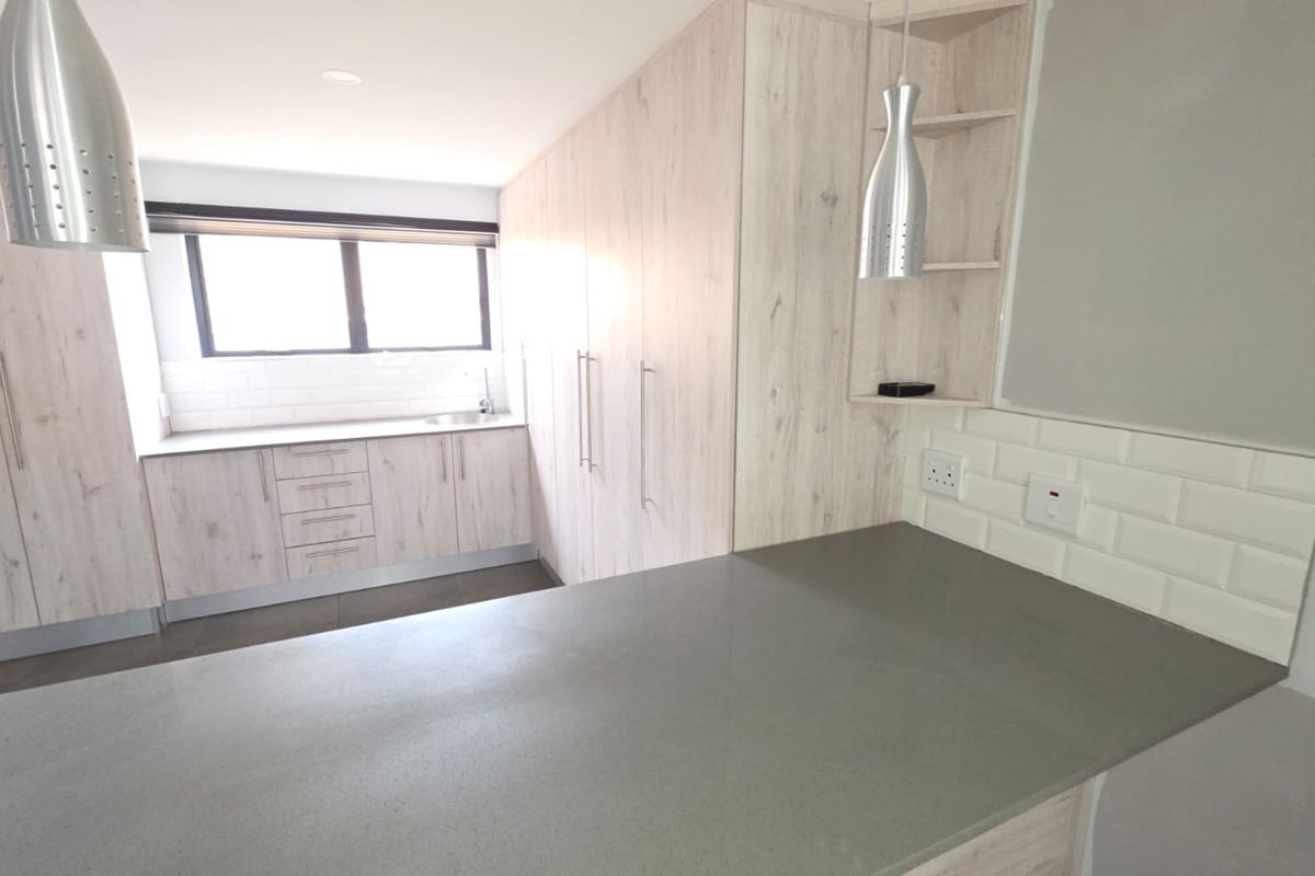 Modern kitchen featuring light wood-grain cabinetry, stone countertops, subway tile backsplash, and a functional breakfast bar area.