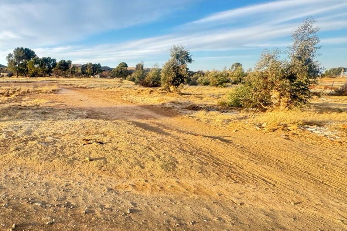 An expansive view of undeveloped residential land featuring natural terrain and native vegetation under a clear blue sky.