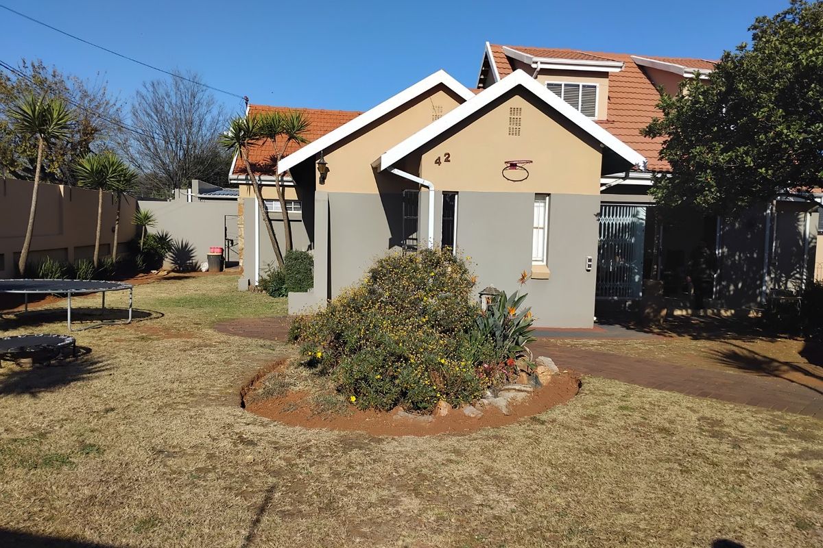 Rear view of the house featuring a tiled roof, paved walkway, and established garden area with perimeter walling.