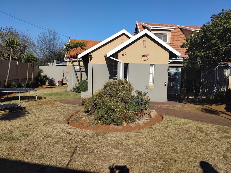 Rear view of the house featuring a tiled roof, paved walkway, and established garden area with perimeter walling.