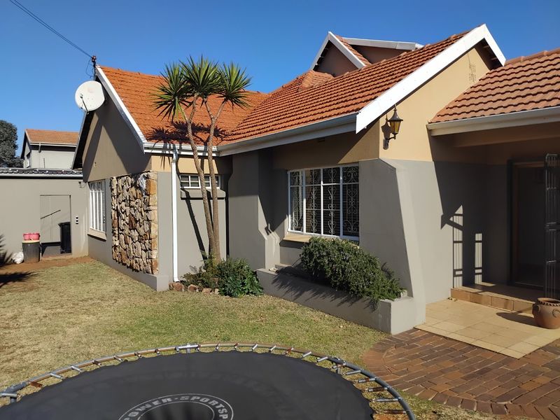 Front elevation of a residential house featuring terracotta roof tiles, stone cladding accents, and a paved entrance area with established garden landscaping.