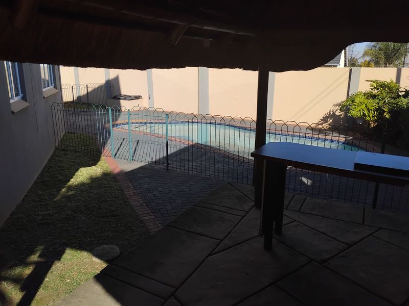 Outdoor entertainment area featuring a covered thatched patio overlooking a swimming pool with paved surrounds and secure perimeter fencing.