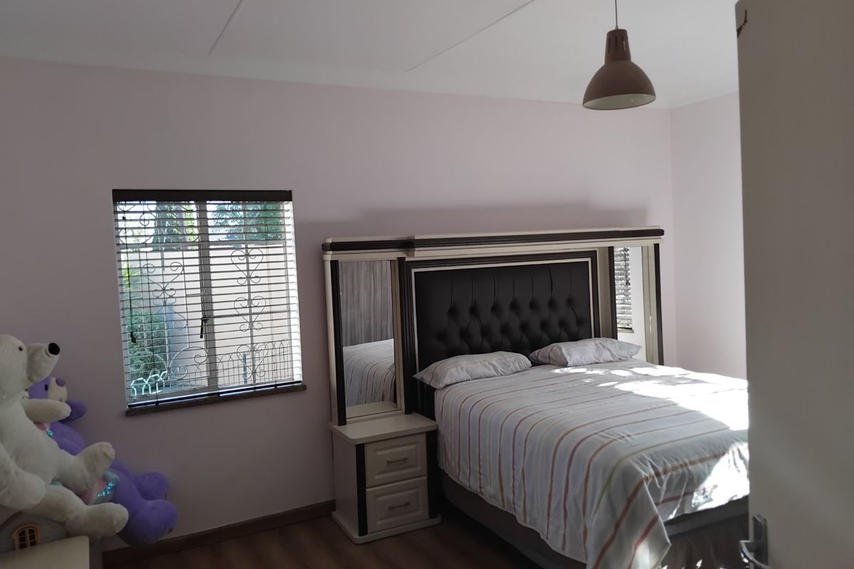 A well-lit bedroom featuring laminate flooring, venetian blinds with security bars, and a central pendant light fixture.