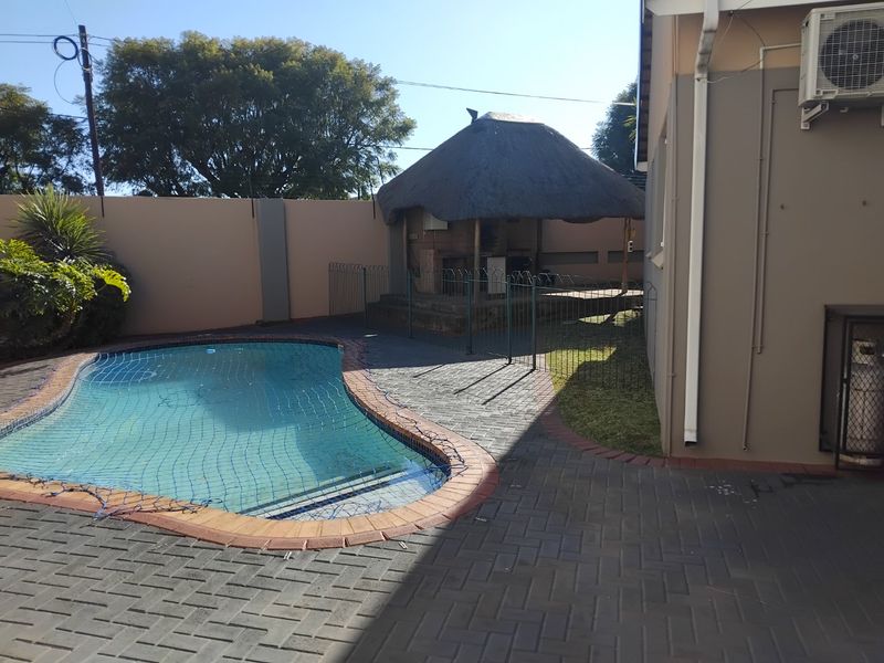 Outdoor pool area featuring a paved patio, a thatched lapa for entertainment, and a secure boundary wall.