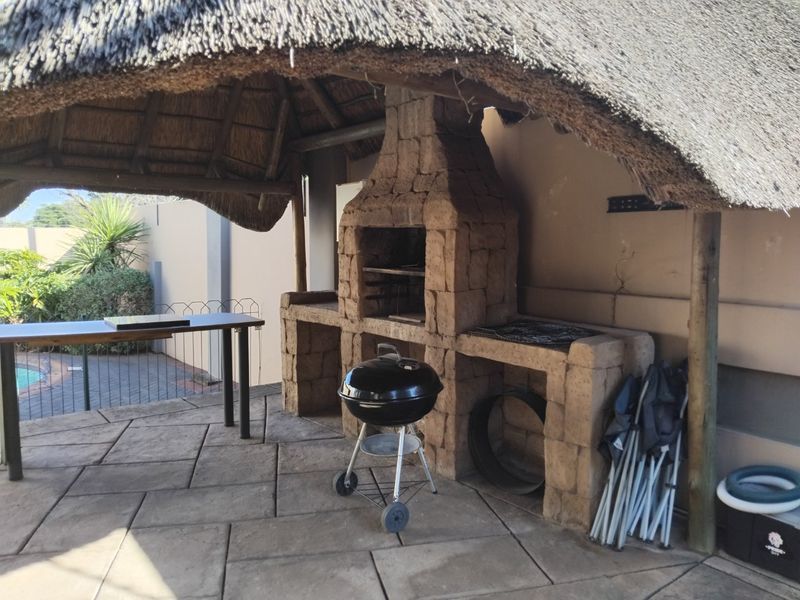 Covered outdoor patio featuring a rustic thatched roof and a substantial stone-clad built-in braai area, perfect for alfresco dining and entertaining.